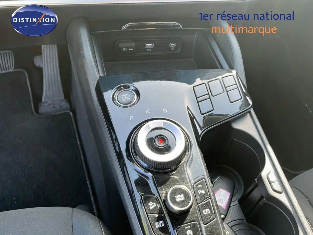 Vue rapprochée de la console centrale noire brillante du Kia Sportage 2022, avec molette de boîte auto et bouton start/stop.