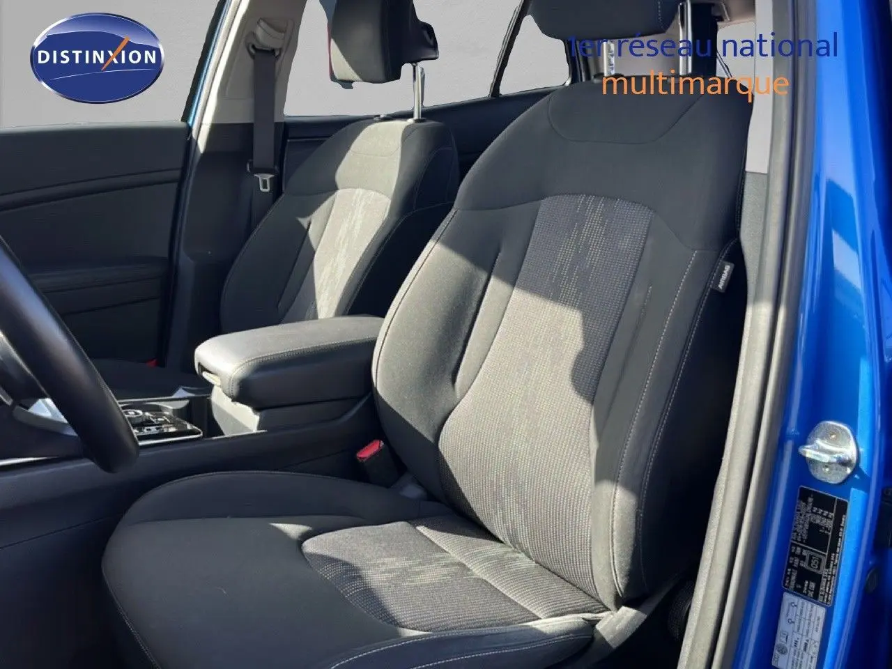 Vue intérieure côté conducteur du Kia Sportage bleu fusion métal 2022, sièges tissu noir avec accoudoir central.