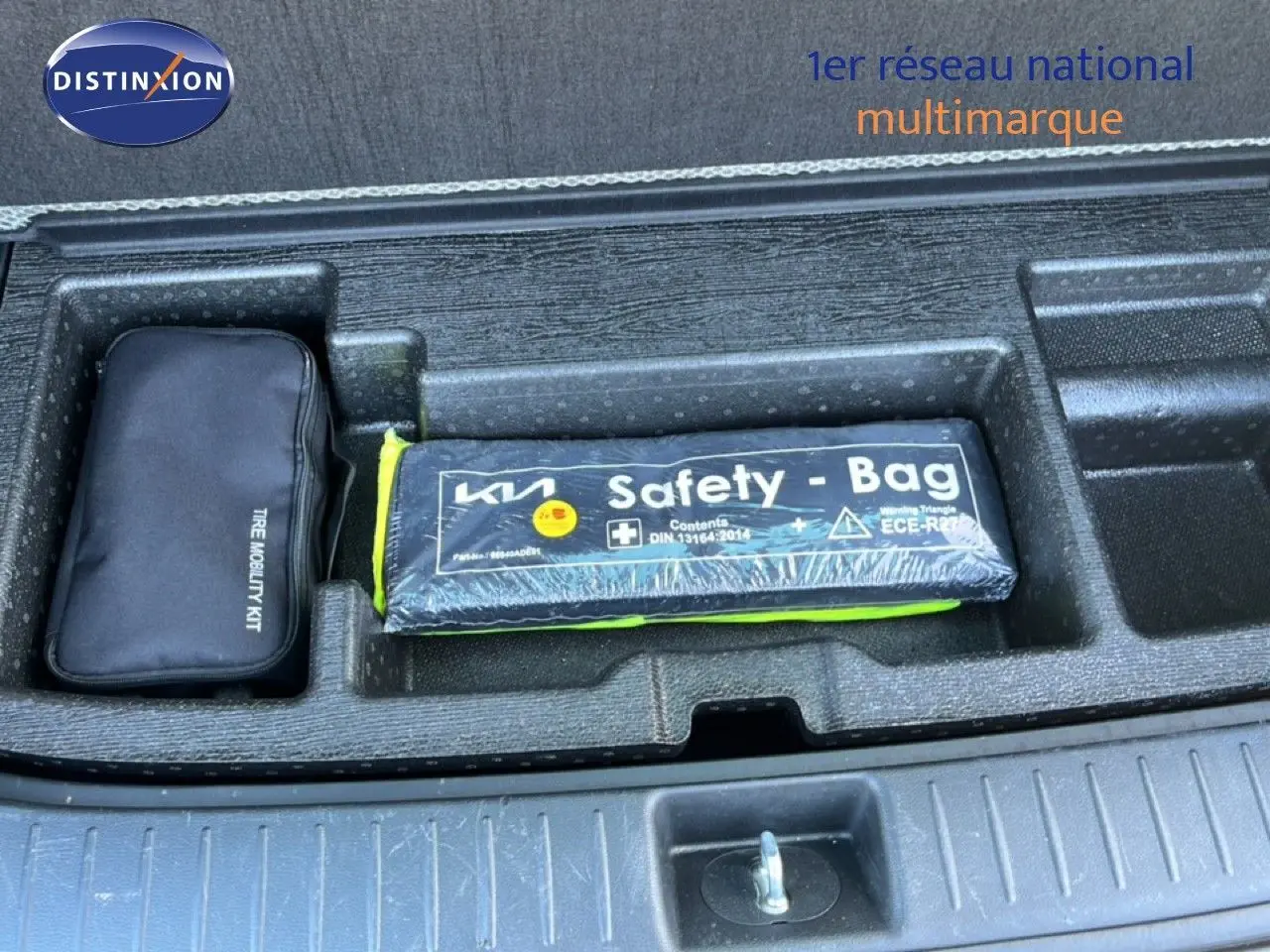 Vue plongeante sur le coffre ouvert d’un Kia Sportage bleu fusion métal, montrant le kit de mobilité et la trousse de sécurité.