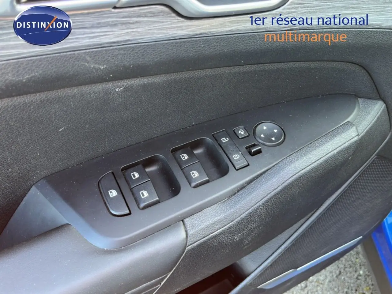 Gros plan sur les commandes des vitres et rétroviseurs sur la porte côté gauche d'un Kia Sportage bleu fusion métal.