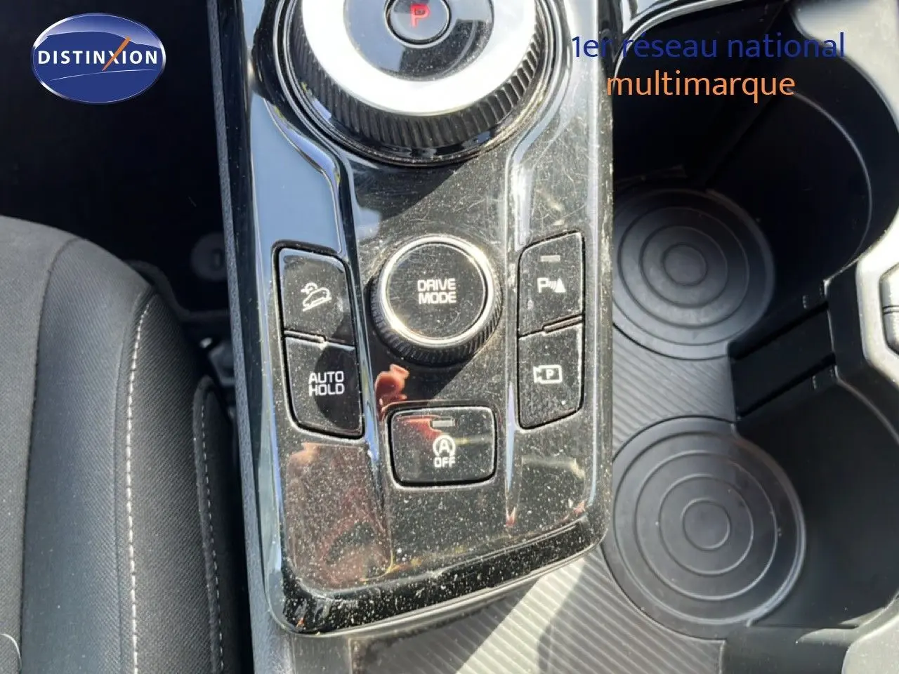 Vue rapprochée de la console centrale noire brillante du Kia Sportage bleu fusion, montrant les commandes de conduite et porte-gobelets.