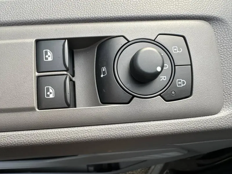 Gros plan sur les commandes de réglage des rétroviseurs et des vitres côté conducteur du Volkswagen Transporter FGN gris 2025.