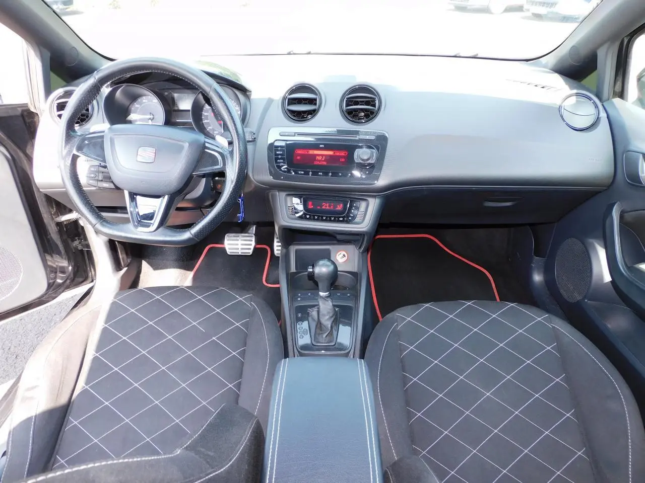 Intérieur avant de la SEAT Ibiza Cupra noire de 2011, volant cuir, console centrale avec levier de vitesse automatique et tapis noirs à liseré rouge.
