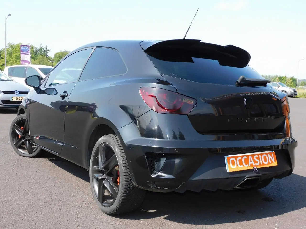 Vue 3/4 arrière droite d'une SEAT Ibiza Cupra noire avec jantes noires et sigle CUPRA sur le coffre.