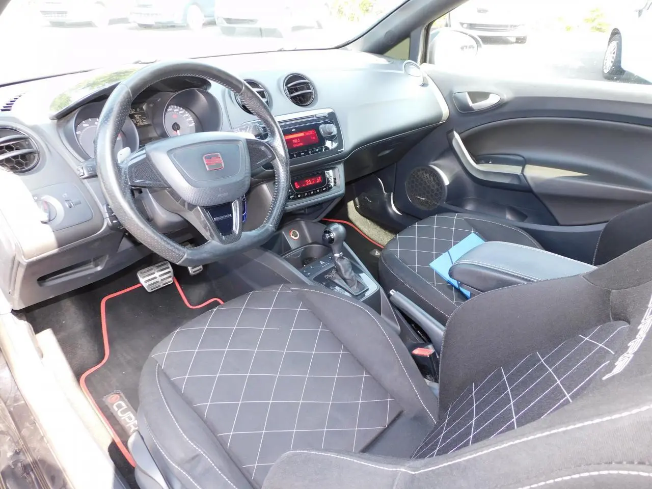 Intérieur de la SEAT Ibiza Cupra 2011 vu côté conducteur, sièges sport noirs avec surpiqûres blanches et volant cuir logoté.