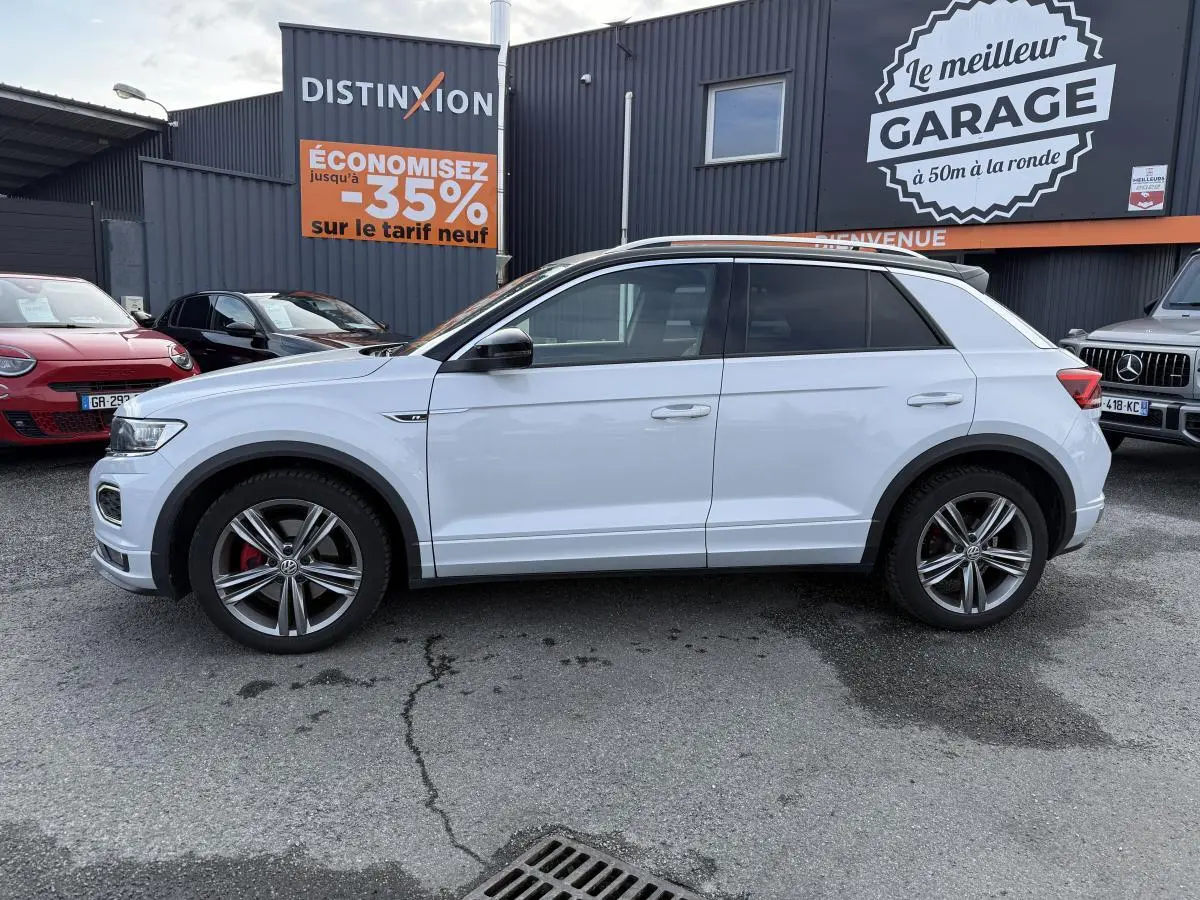 Volkswagen T-Roc blanc vue de profil côté gauche, jantes alliage 18 pouces et détails R-Line visibles.