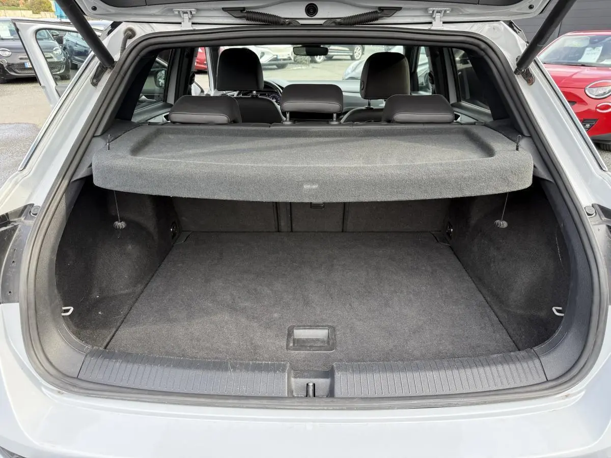 Coffre ouvert vu de l'arrière d'un Volkswagen T-Roc gris avec cache-bagages et sièges arrière visibles.