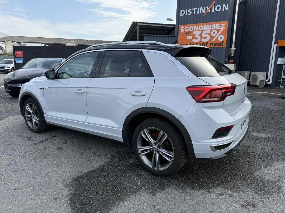 Volkswagen T-Roc blanc en vue 3/4 arrière côté gauche, avec jantes alliage et toit noir contrastant.