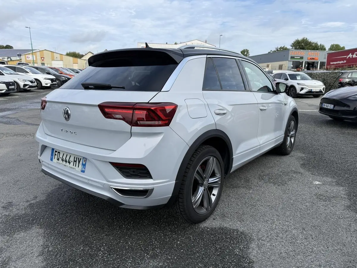 Volkswagen T-Roc blanc vue 3/4 arrière droit avec toit noir et jantes alliage sur parking.