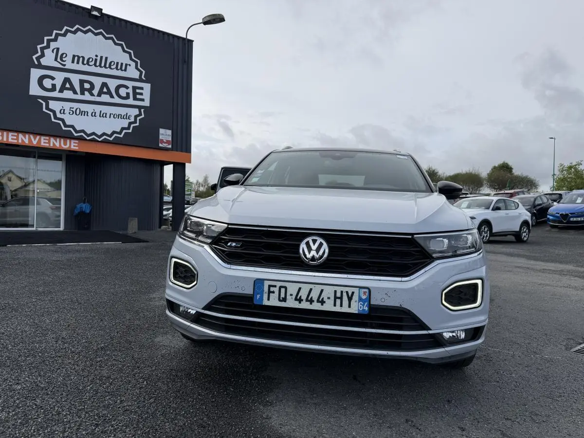 Vue frontale d'un Volkswagen T-Roc gris avec calandre noire et feux LED en forme de losange allumés.
