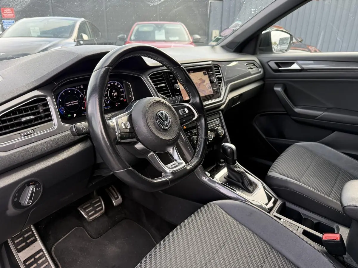 Intérieur avant du Volkswagen T-Roc 1.5 TSI gris, vue côté conducteur avec volant cuir et tableau de bord digital.