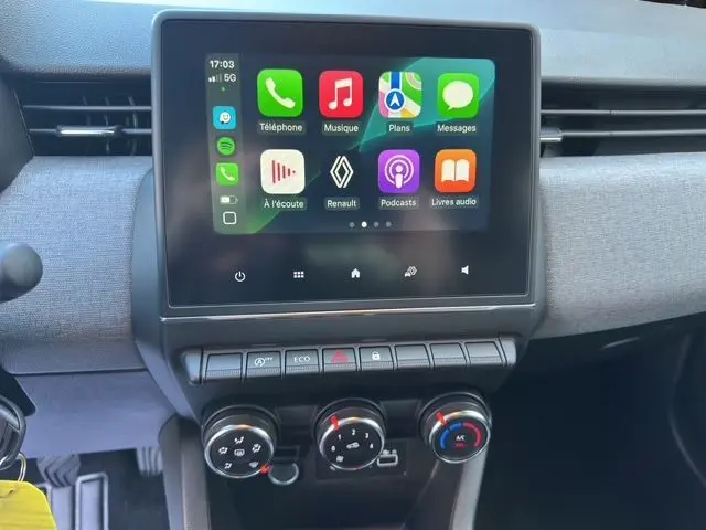 Vue rapprochée de la console centrale de la Renault Clio V 2025, écran tactile avec interface Apple CarPlay et commandes climatisation.