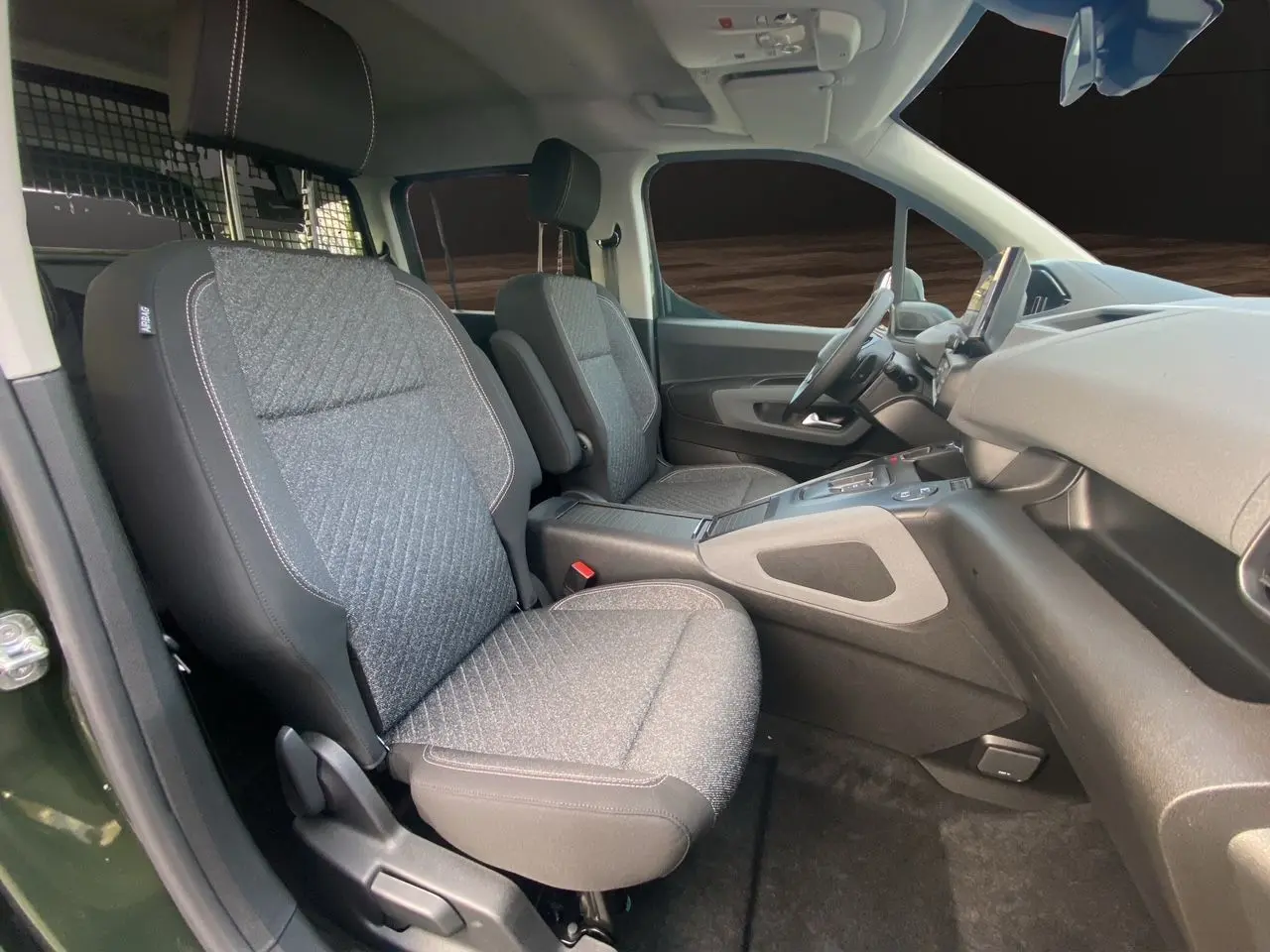 Vue intérieure côté conducteur du Peugeot Rifter 2025 vert Sirkka Green, sièges tissu gris et tableau de bord moderne.