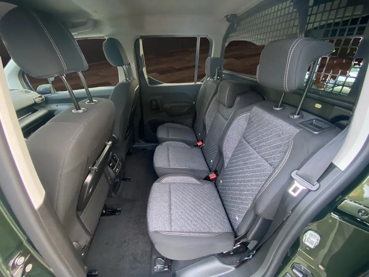 Vue intérieure côté droit du Peugeot Rifter 2025 vert Sirkka, montrant les sièges arrière en tissu gris avec grille de séparation.