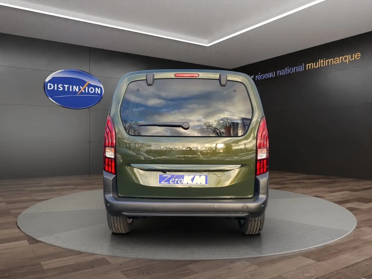 Vue arrière du Peugeot Rifter 2025 vert Sirkka avec hayon vitré et feux verticaux rouges en intérieur showroom.