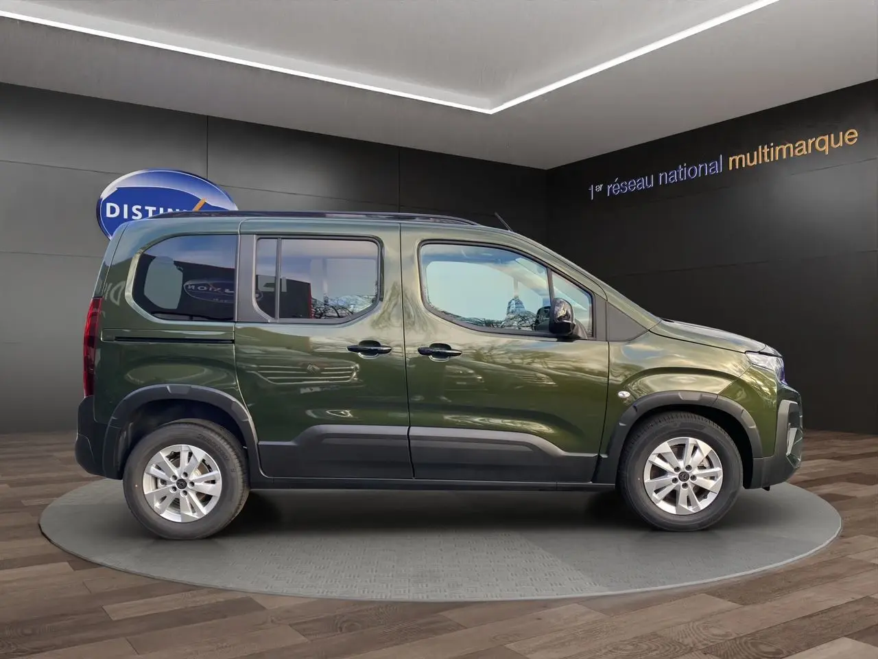 Profil droit du Peugeot Rifter 2025 vert Sirkka avec jantes alliage 16'' et barres de toit noires en showroom.