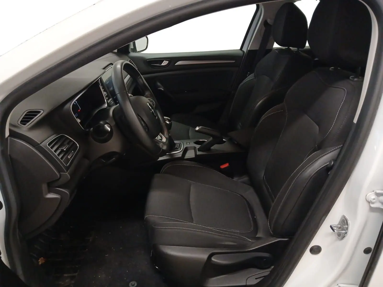 Vue intérieure côté conducteur de la Renault Mégane IV blanche, montrant les sièges noirs et le tableau de bord.