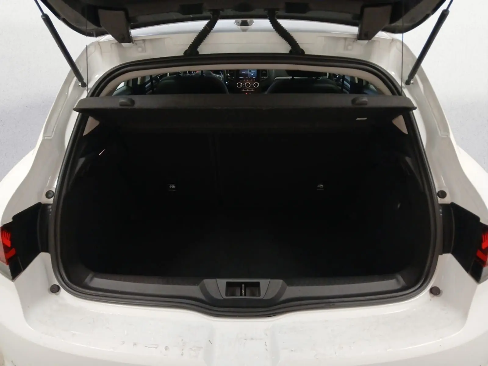 Coffre ouvert vu de l'arrière d'une Renault Mégane IV blanche, avec intérieur noir et tablette de coffre relevée.