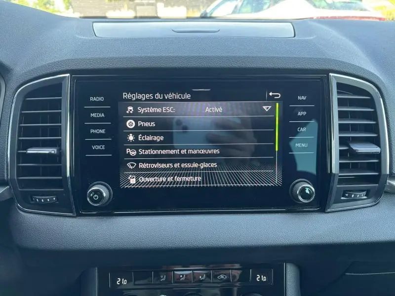 Écran tactile central du tableau de bord du Skoda Karoq blanc, affichant les réglages du véhicule en intérieur.