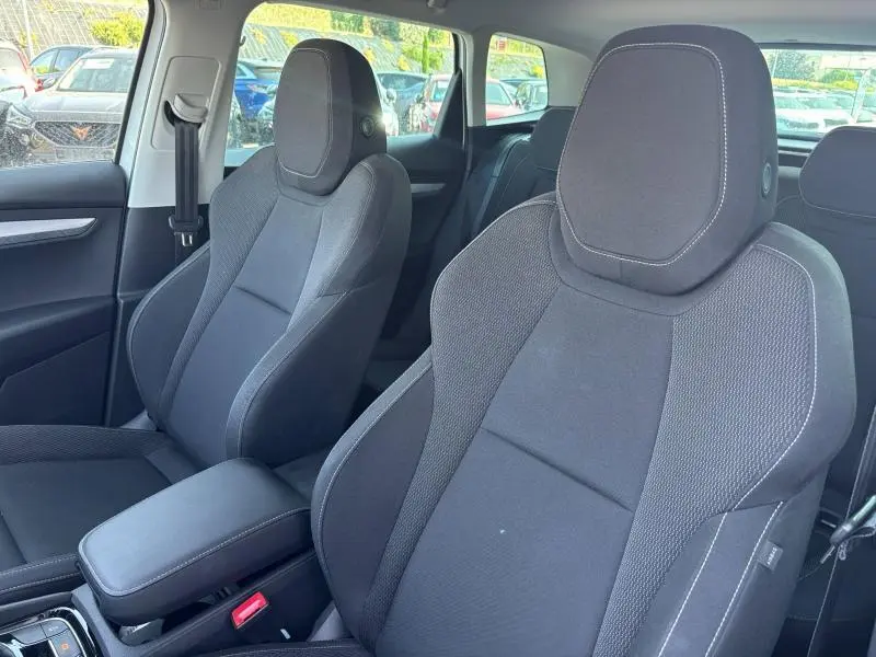 Vue intérieure rapprochée des sièges avant noirs en tissu du Skoda Karoq 2024, avec accoudoir central et ceinture côté gauche visible.