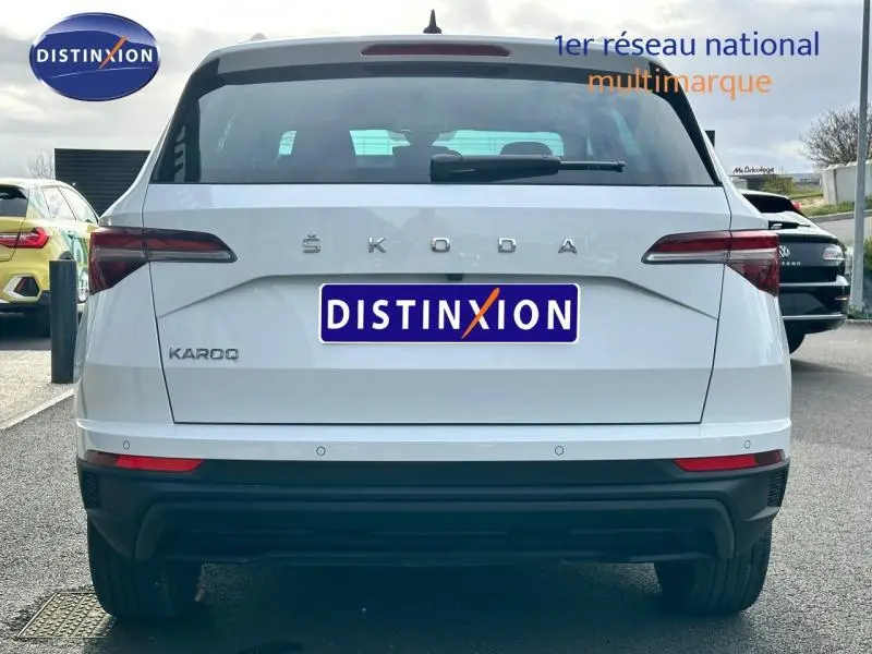 Vue arrière d'un Skoda Karoq blanc lune métallisée avec feux arrière LED et logo distinctif SKODA visible.