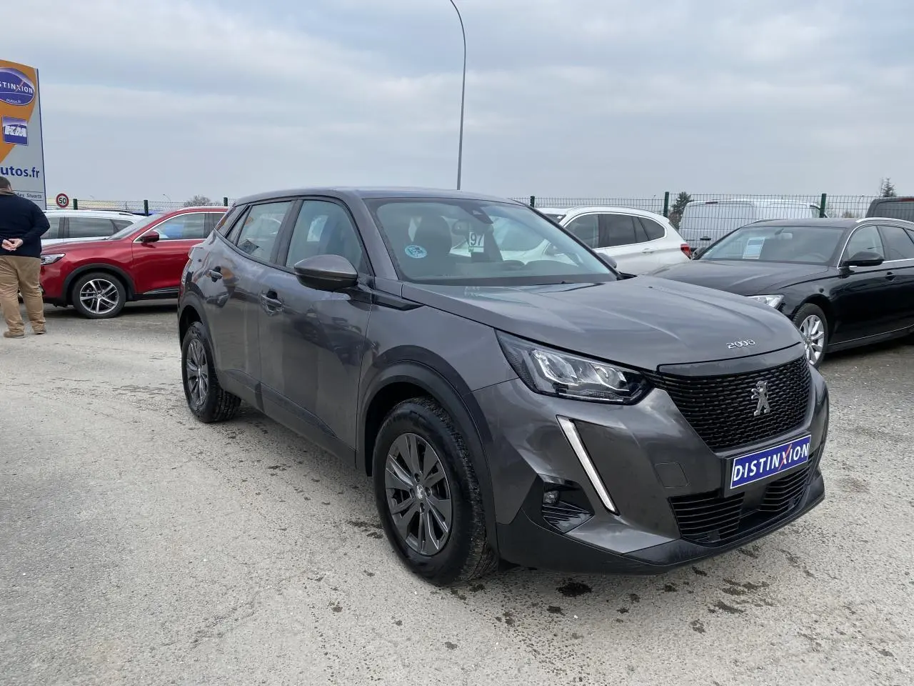 Peugeot 2008 gris foncé vue 3/4 avant droit sur parking avec calandre noire et feux LED griffés.