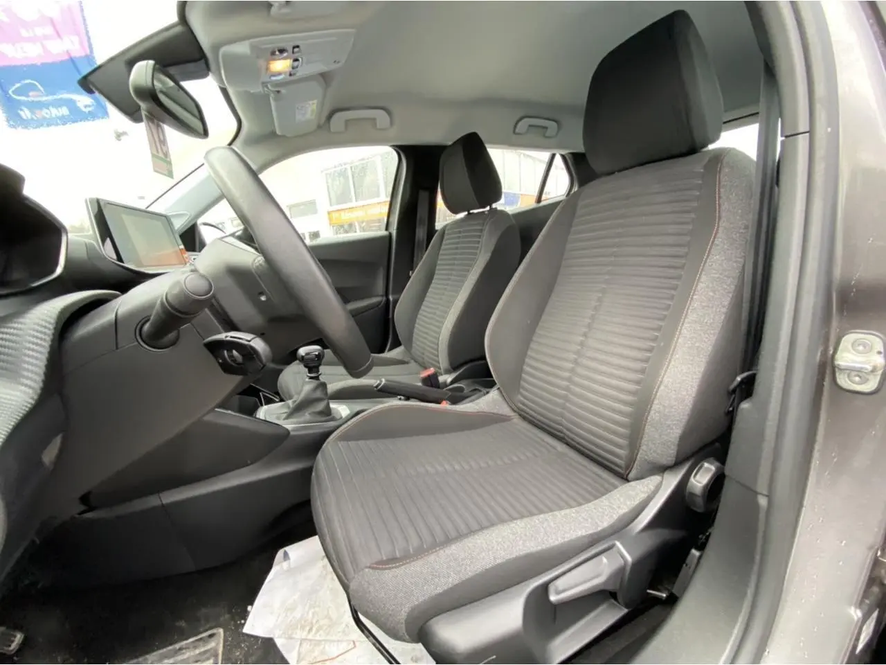 Intérieur avant droit du Peugeot 2008 gris foncé 2021, sièges tissu gris avec surpiqûres, volant et levier de vitesse manuels visibles.