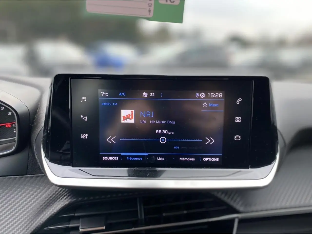 Écran tactile central du Peugeot 2008 2021 affichant la radio NRJ, avec tableau de bord en carbone gris foncé.