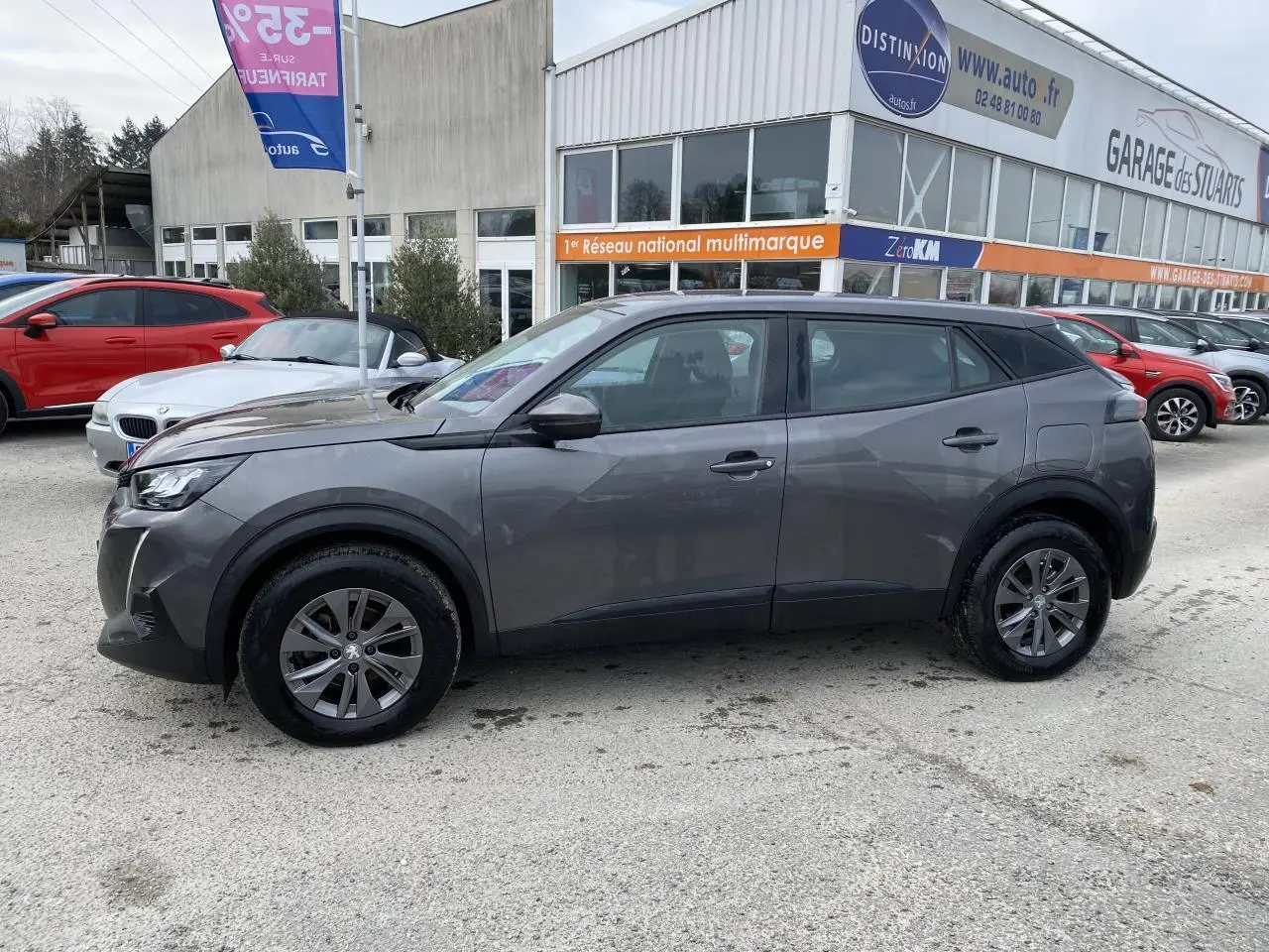 Profil côté gauche d'un Peugeot 2008 gris foncé métallisé garé devant un garage multimarque.