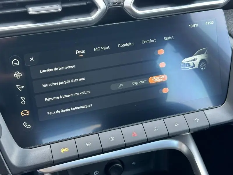 Écran tactile du tableau de bord du MG ZS blanc 2025 affichant les réglages des feux et assistances à la conduite.
