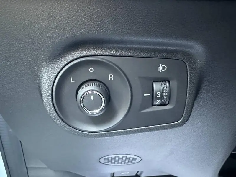 Gros plan sur les commandes noires de réglage des rétroviseurs et des phares du MG ZS Hybrid+ blanc 2025.