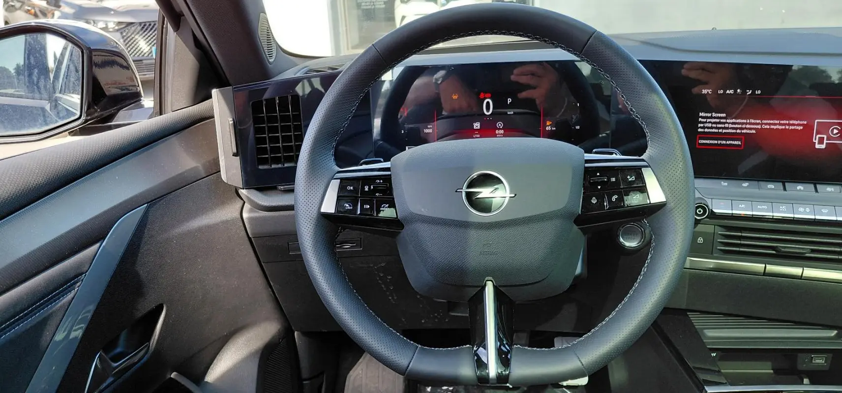 Vue intérieure centrée sur le volant cuir noir de l'Opel Astra 2025 avec tableau de bord digital et écran tactile.