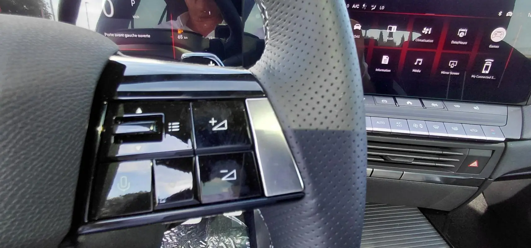 Gros plan sur les commandes au volant en cuir perforé de l’Opel Astra 2025, avec écran tactile et console centrale visible.