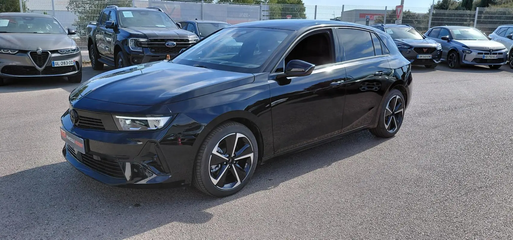 Opel Astra noire vue en 3/4 avant droit, vitres surteintées et jantes alliage 17 pouces distinctives.