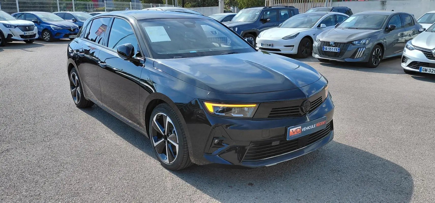 Opel Astra noire vue 3/4 avant droit, avec jantes alliage 17 pouces et feux diurnes allumés.