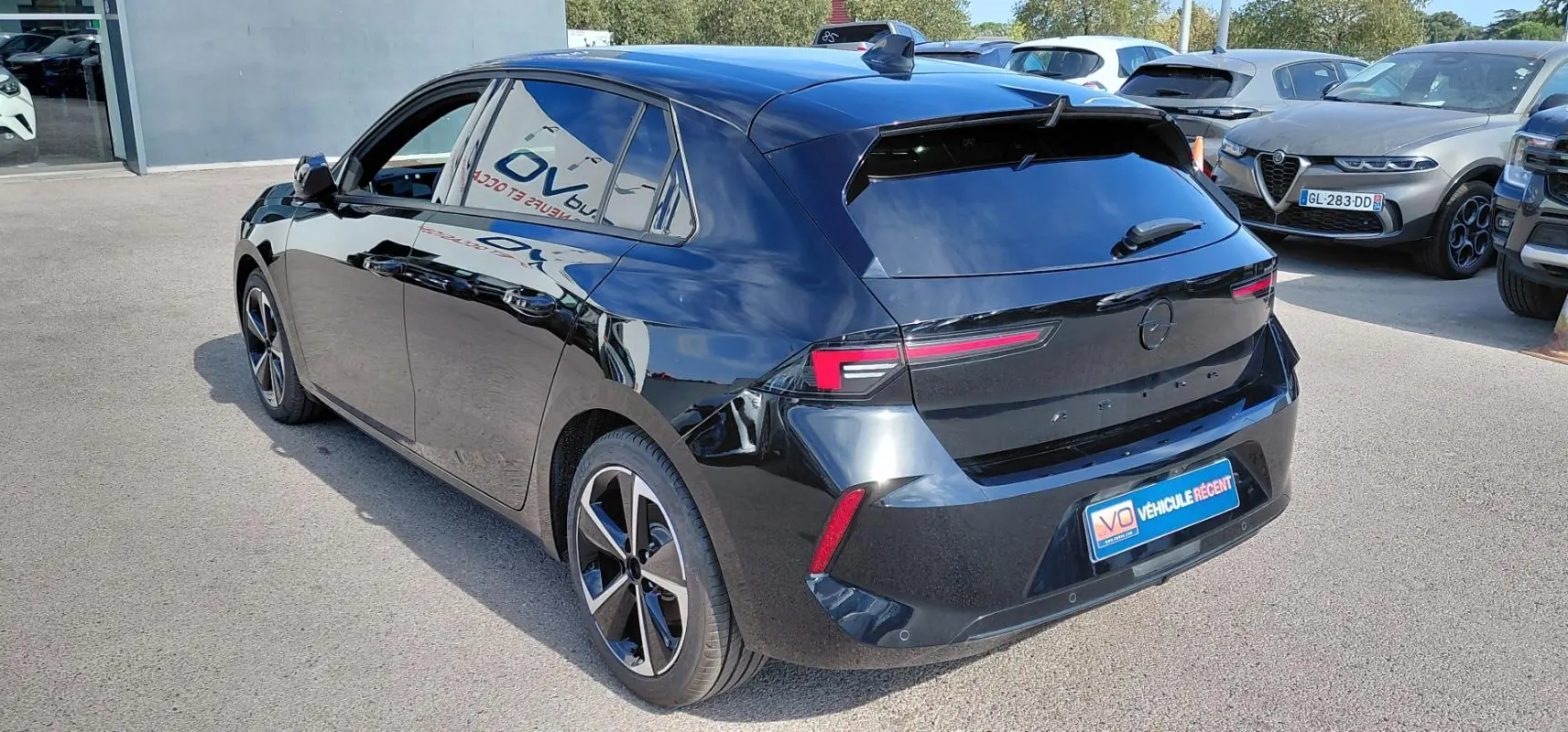 Opel Astra noire vue 3/4 arrière droit, avec jantes alliage 17 pouces et vitres surteintées.