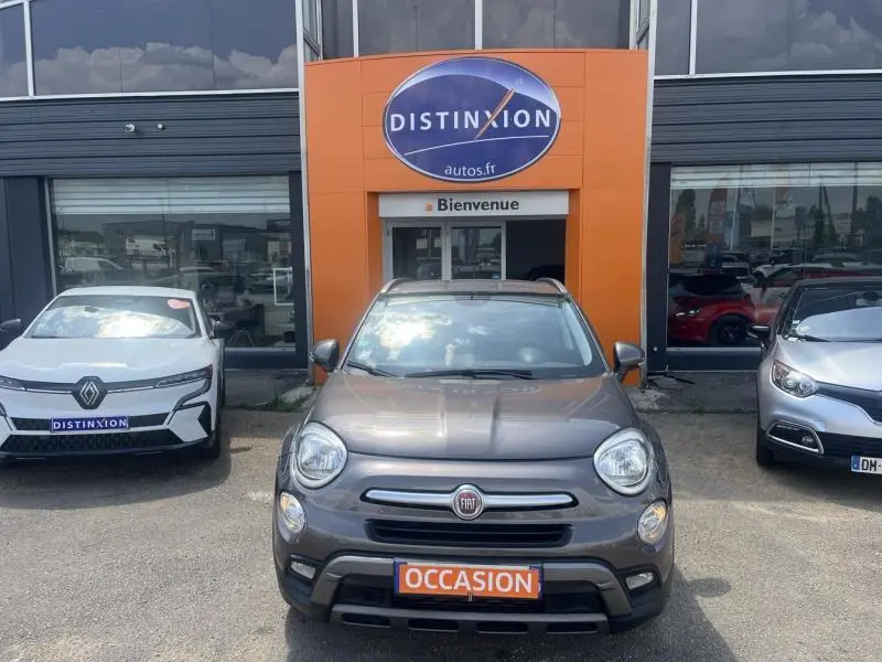 Vue avant d'une FIAT 500X bronze métallisé stationnée devant un concessionnaire avec plaque "OCCASION" visible.
