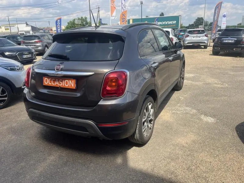 Vue 3/4 arrière droite d'une Fiat 500X bronze métallisé avec vitres surteintées sur un parking extérieur.