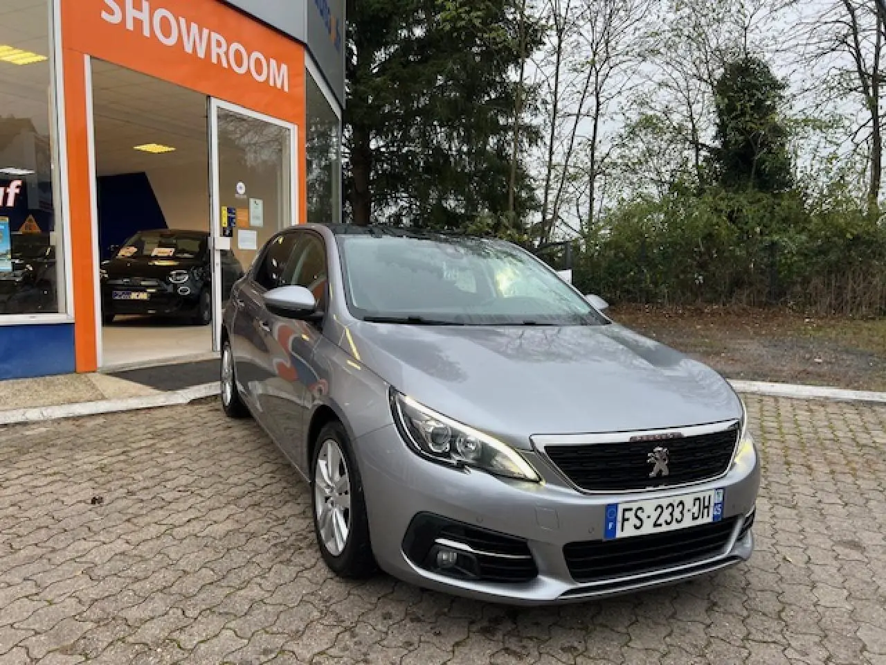 Peugeot 308 gris artense vue 3/4 avant droit devant un showroom avec toit panoramique en verre.