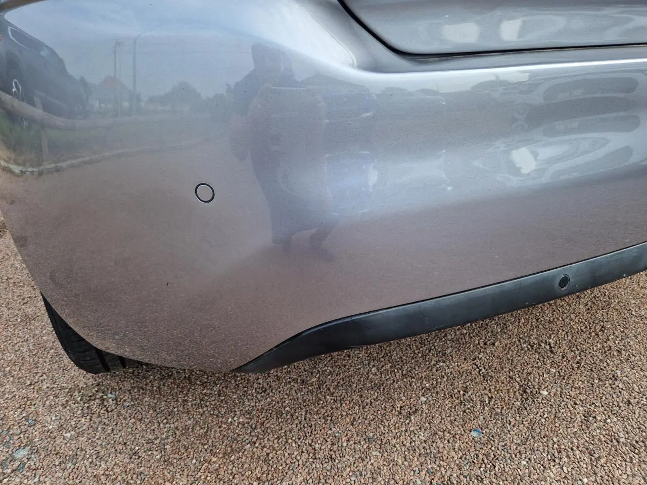 Gros plan sur le pare-chocs arrière gris artense de la Peugeot 308 avec capteur de stationnement visible.