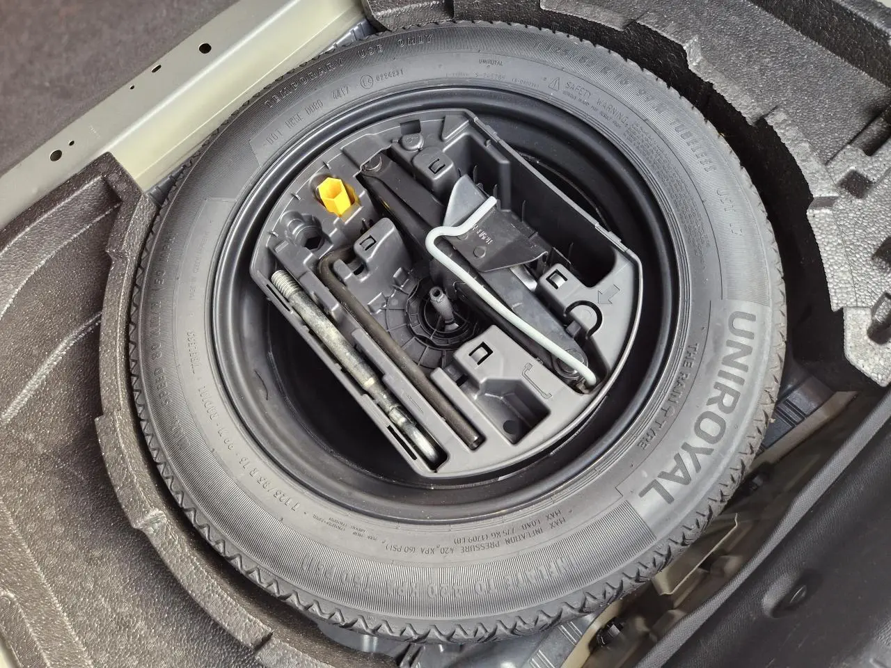 Gros plan sur la roue de secours galette et son kit d'outils dans le coffre d'une Peugeot 308 gris Artense.
