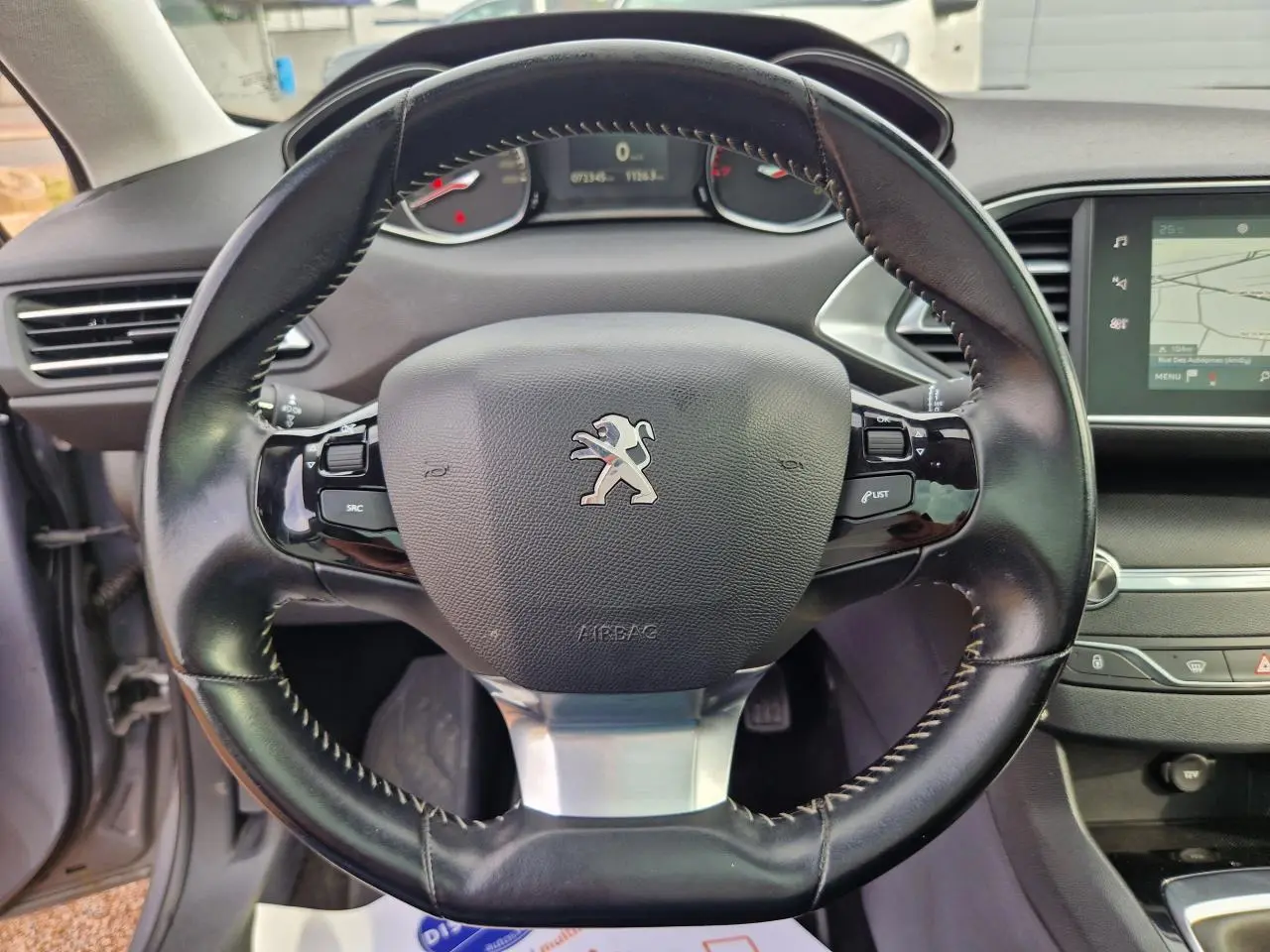 Vue rapprochée du volant cuir noir avec logo Peugeot, tableau de bord et écran tactile de la Peugeot 308 gris artense.