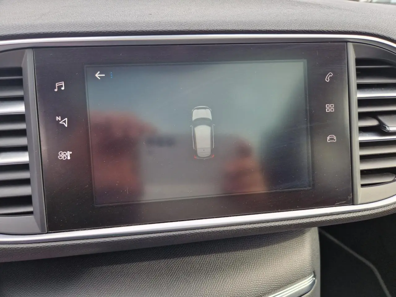 Écran central tactile de la Peugeot 308 gris artense montrant l'aide au stationnement avec vue du dessus du véhicule.