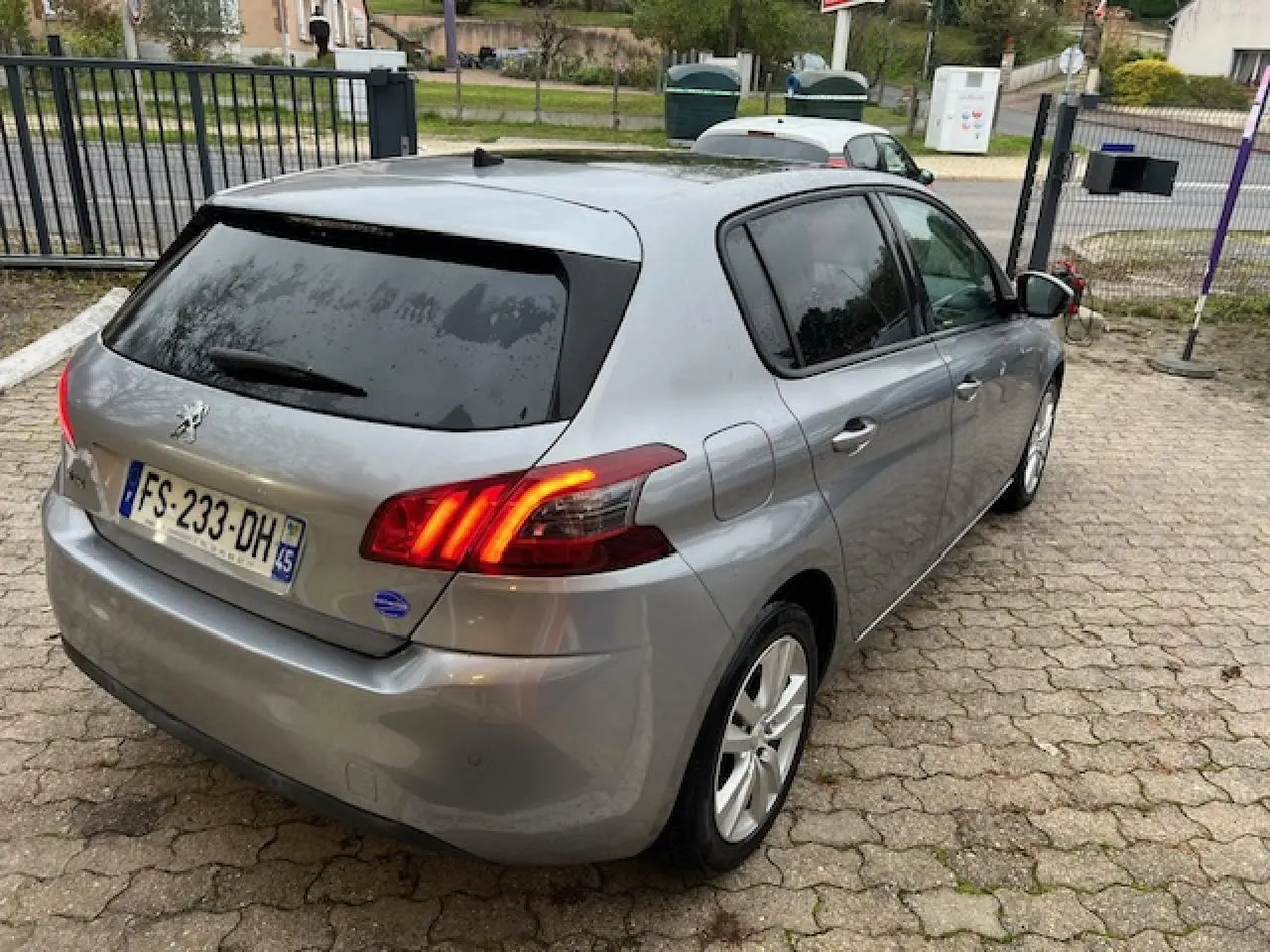 Vue 3/4 arrière droite d'une Peugeot 308 gris artense avec feux arrière allumés et vitres teintées.