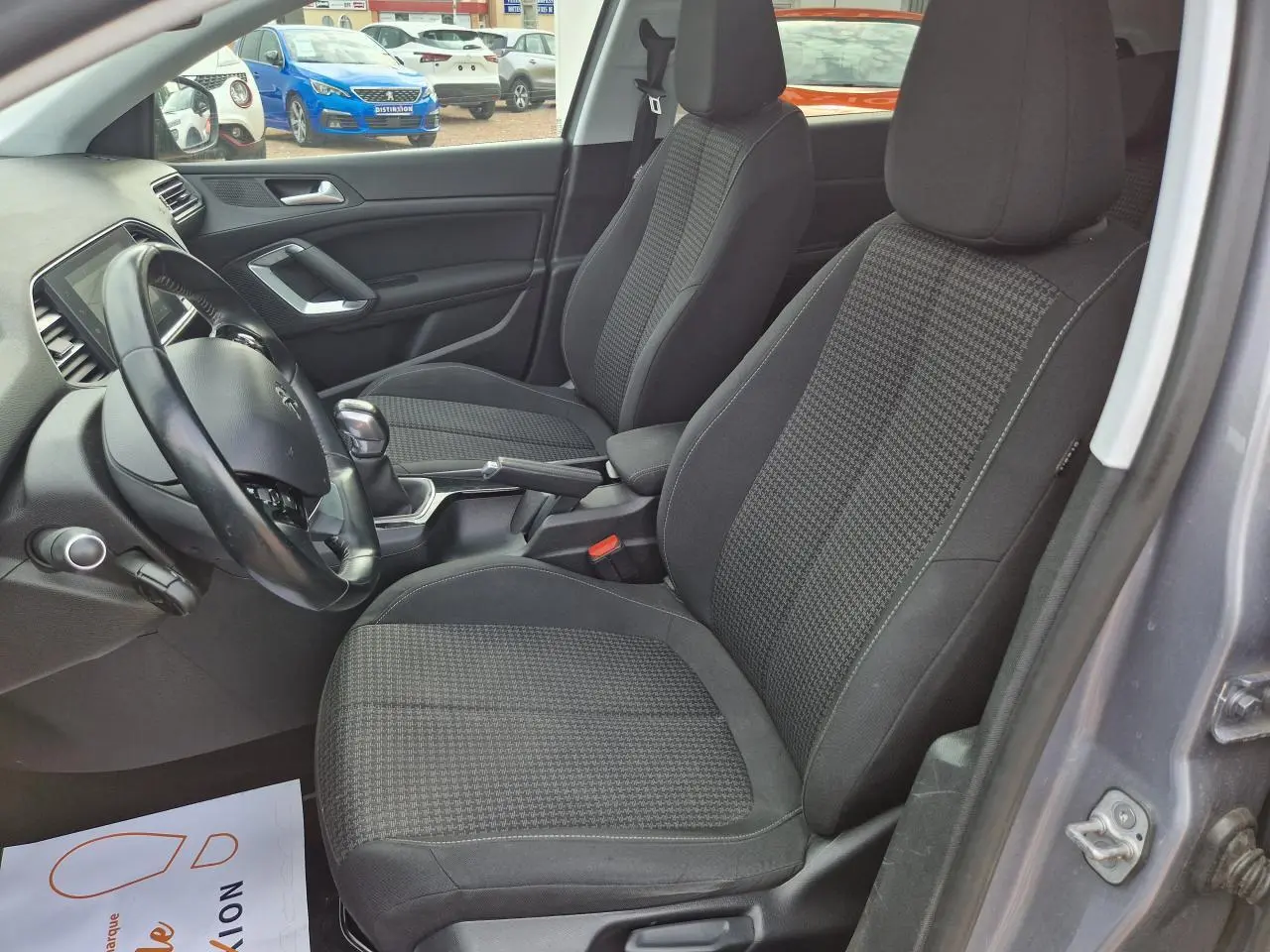 Intérieur de la Peugeot 308 gris artense, vue côté gauche montrant les sièges avant et le volant noir.