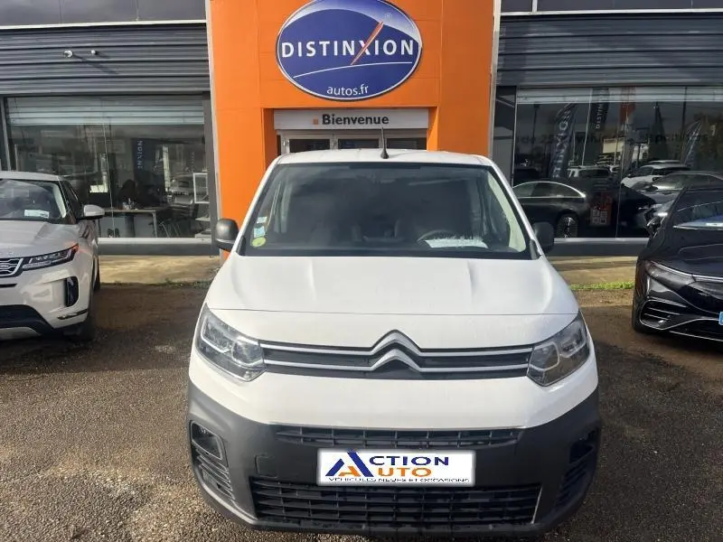 Vue de face d'un Citroën Berlingo Fourgon blanc Banquise avec calandre noire et pare-chocs gris devant un garage.