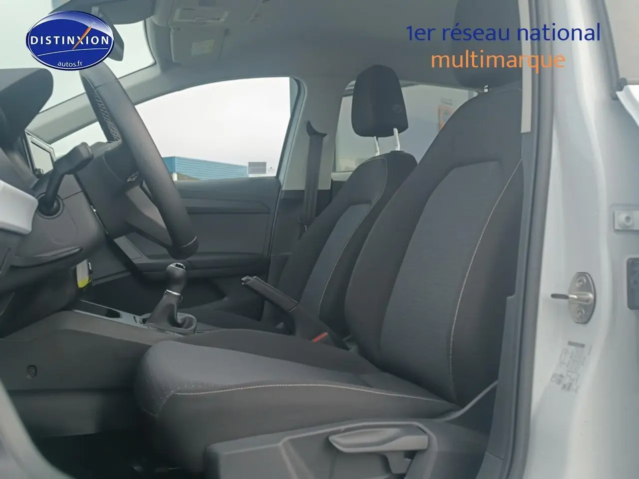 Vue intérieure côté conducteur de la SEAT Ibiza blanc Nevada 2025, sièges tissu gris et volant cuir méplat.