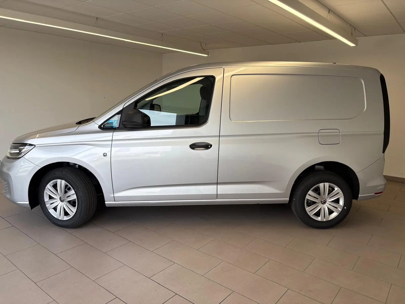 Vue de profil côté gauche du Volkswagen Caddy 1.5 TSI Business 2025 en gris argent, fourgon compact sans vitres latérales arrière.