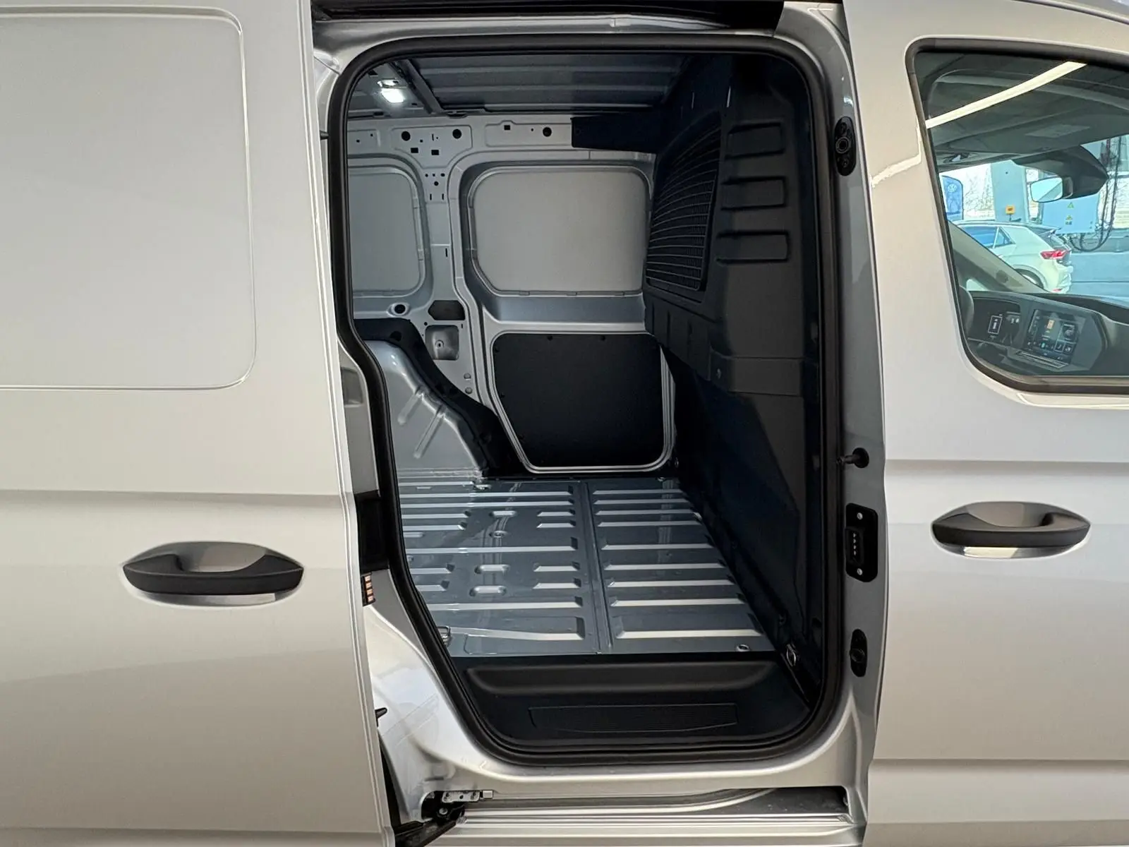 Vue latérale droite du Volkswagen Caddy 2025 gris argent avec porte coulissante ouverte montrant l'espace de chargement vide.
