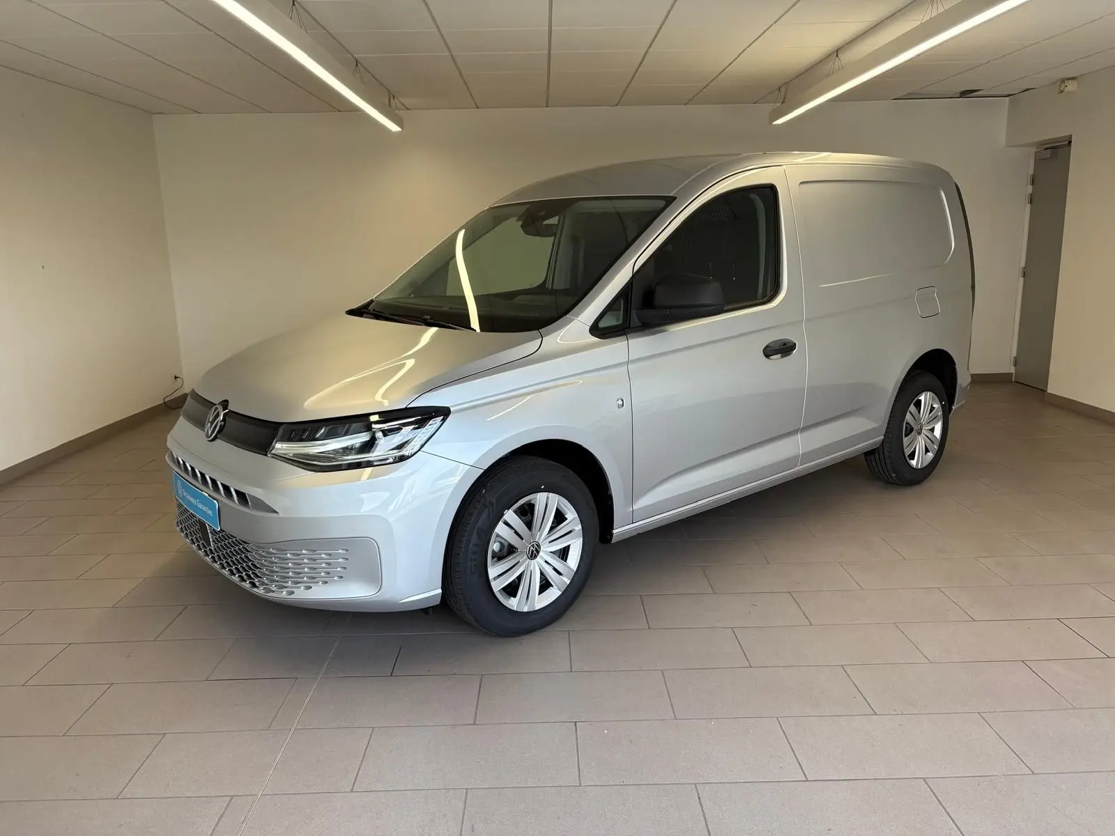 Vue 3/4 avant droit d'un Volkswagen Caddy 2025 gris argent, utilitaire compact avec calandre moderne et jantes simples.